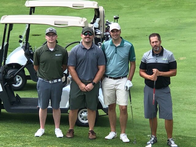 four men standing in front of a golf course on green grass
